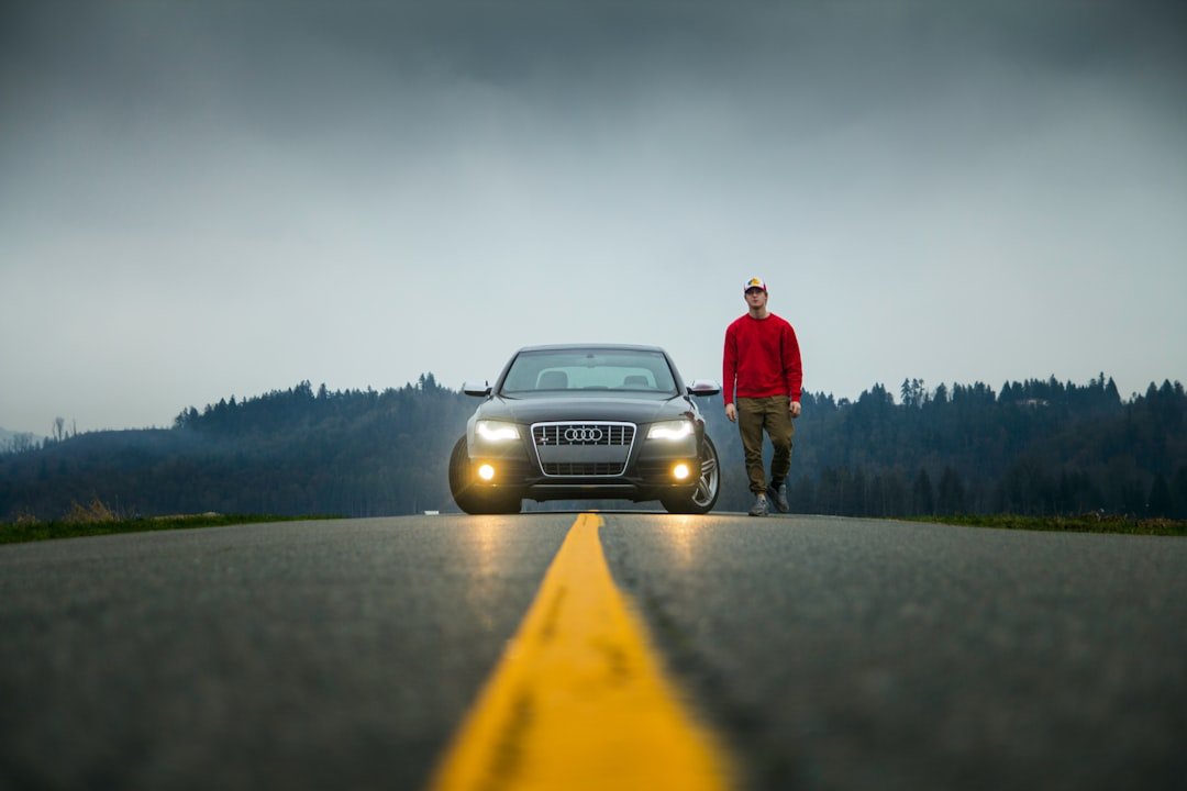 man in red jacket standing beside black car on road during daytime