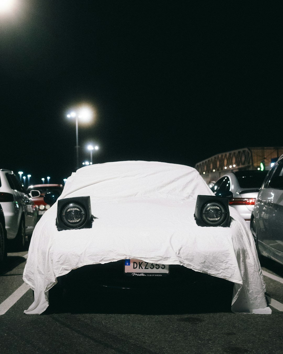 Car covered in white sheet with pop-up headlights visible
