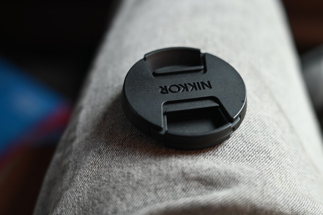 A nikon lens cap sits on a person's leg.