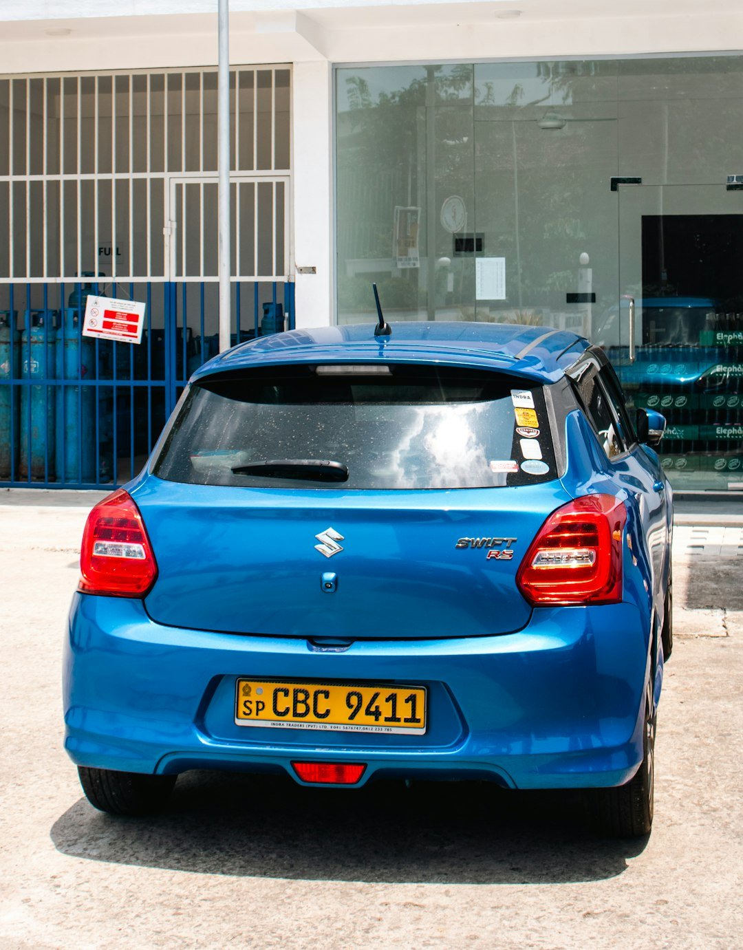 A blue suzuki swift parks in front of a building.