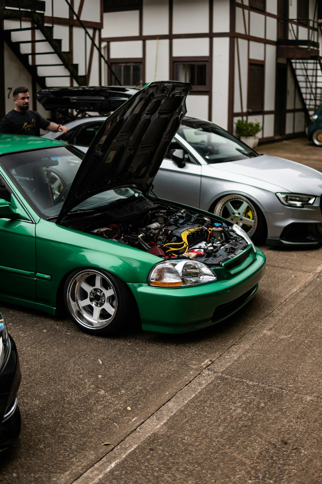 Green car with hood open, silver car behind