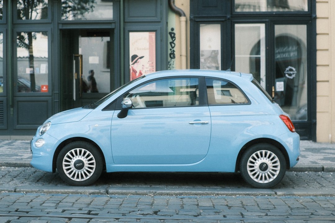 A light blue fiat 500 parked on the street.