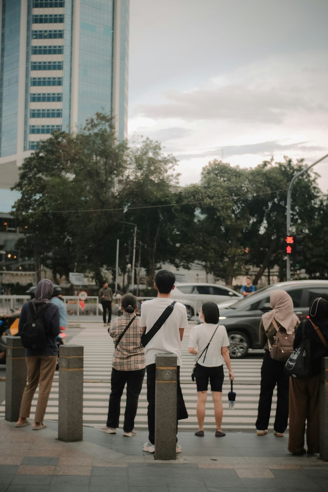 People wait to cross a busy city street at dusk.