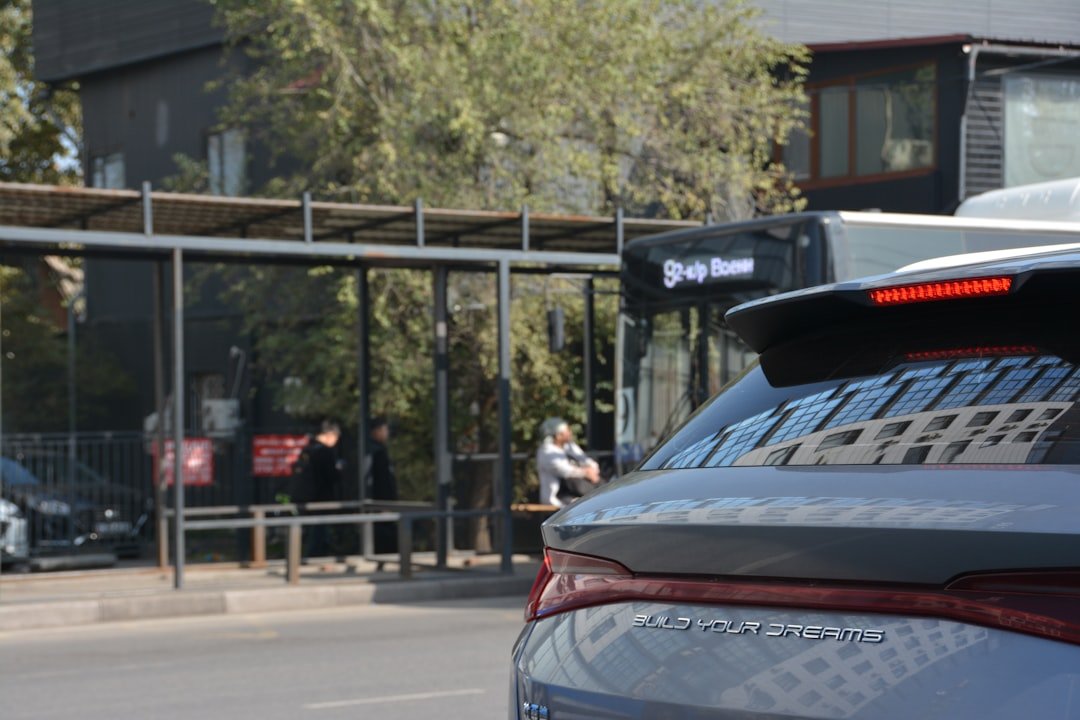 People wait at a bus stop behind a car.