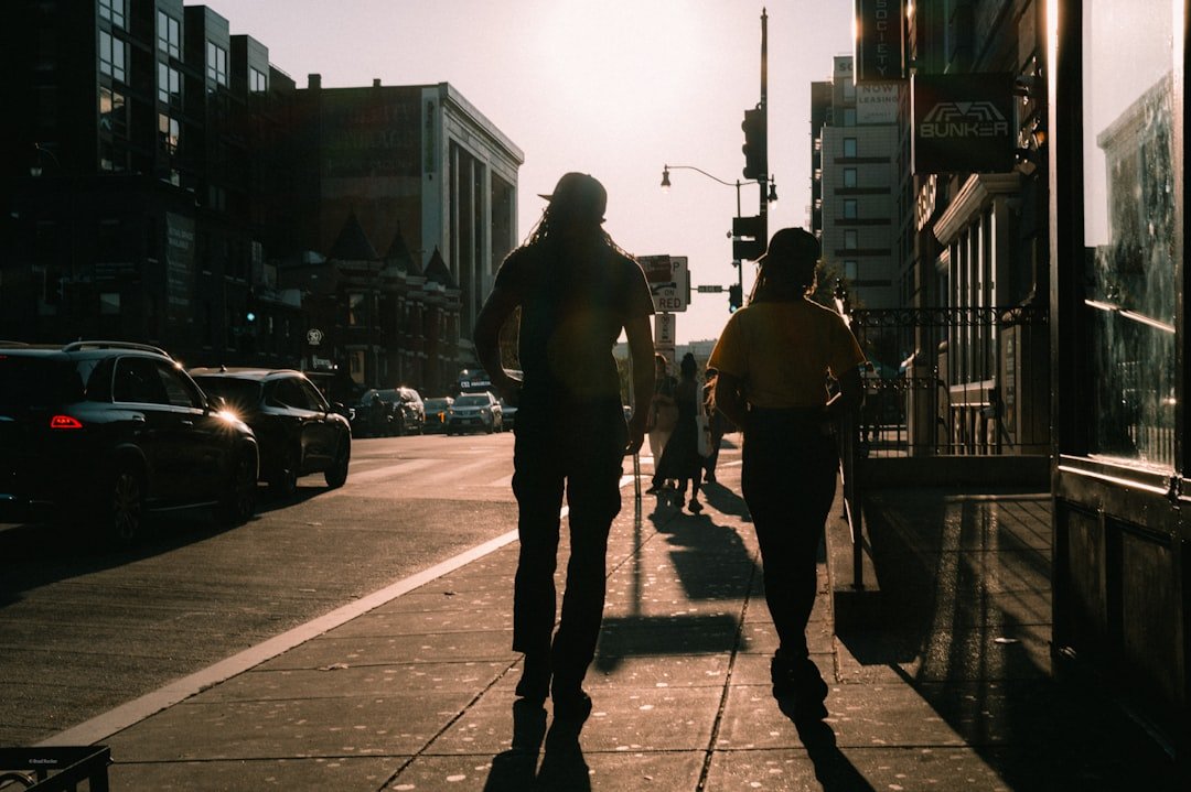 Two people walk down a sunlit city sidewalk.