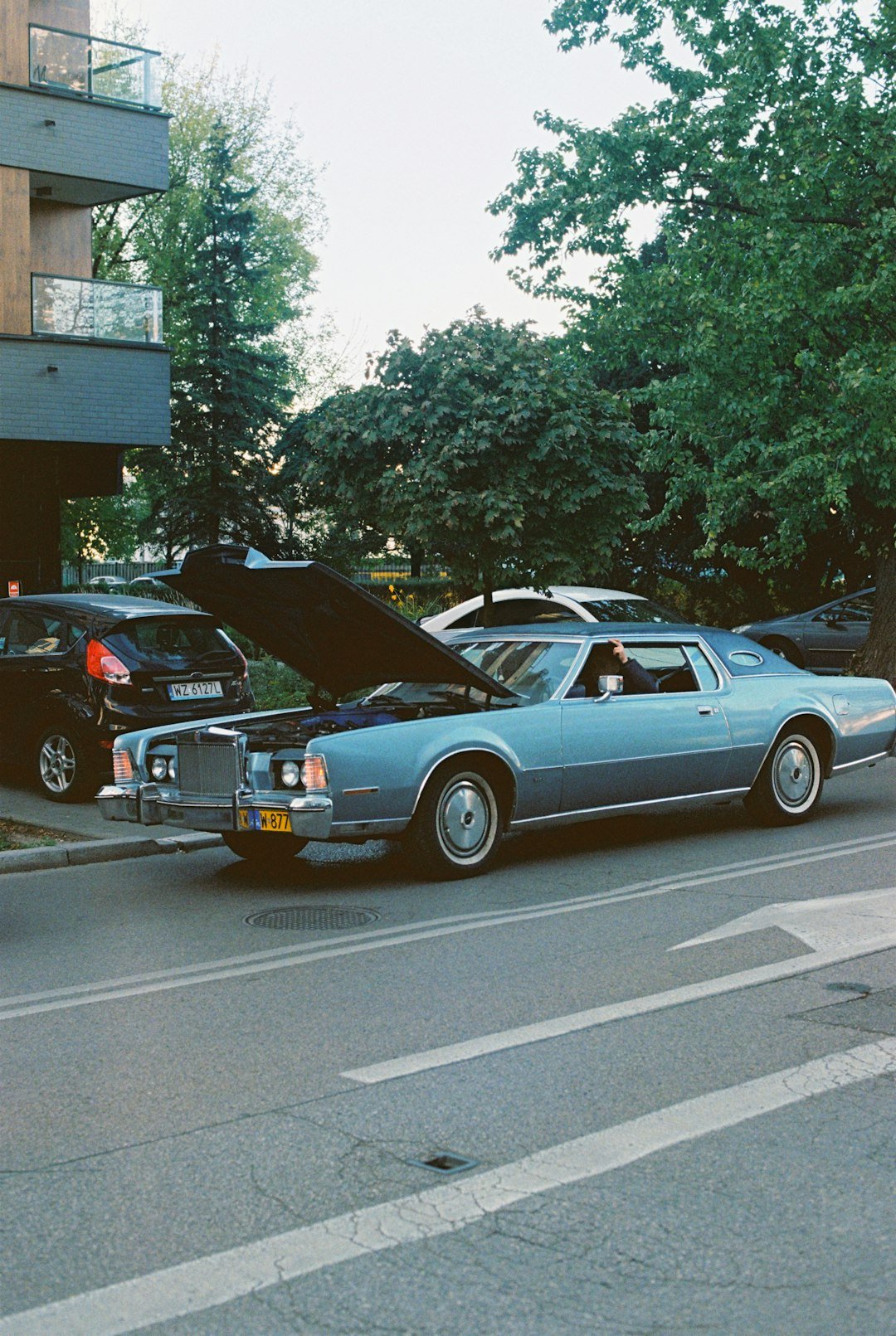 A blue classic car has its hood open.