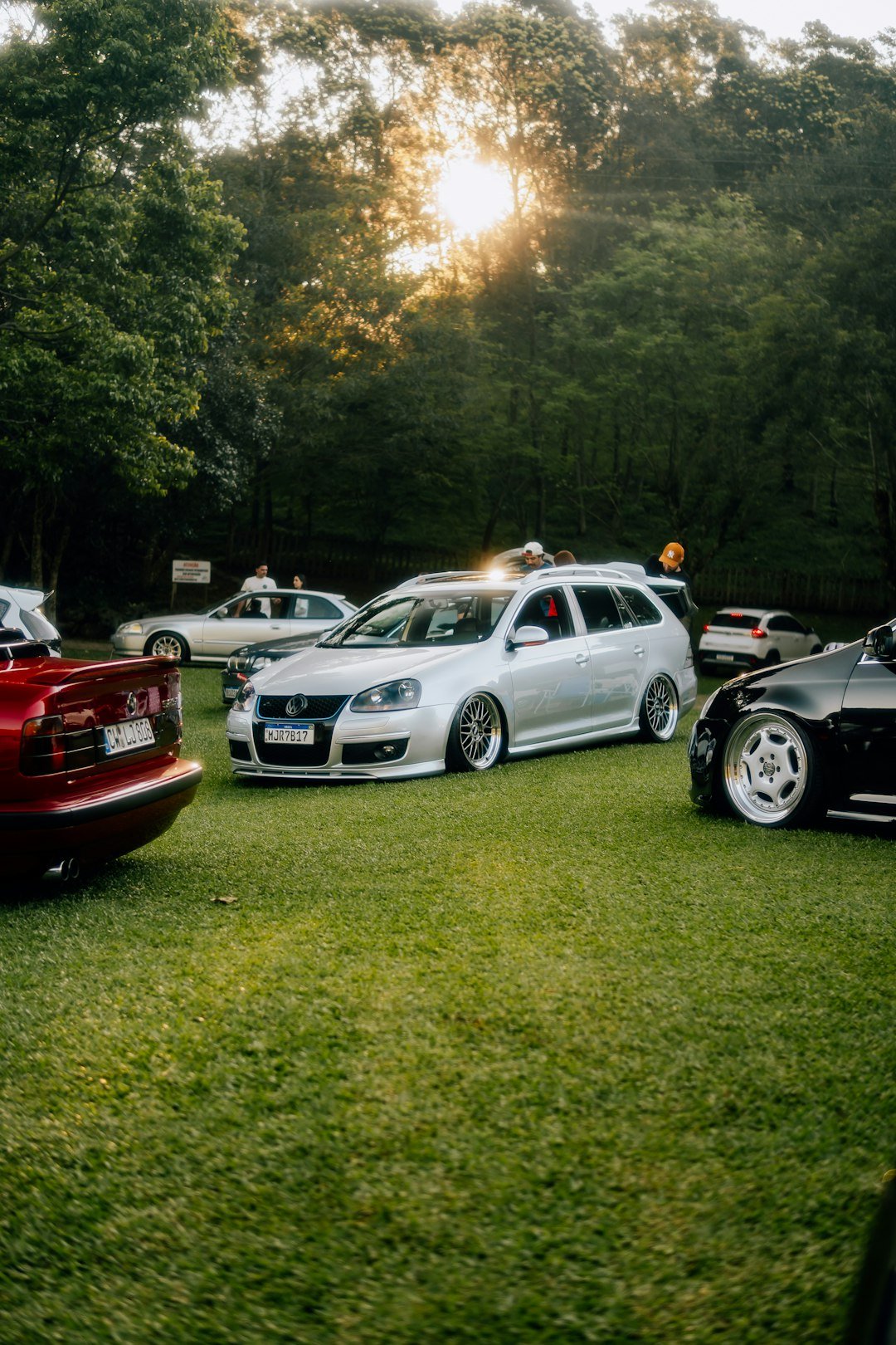 Cars parked on a grassy field at sunset.
