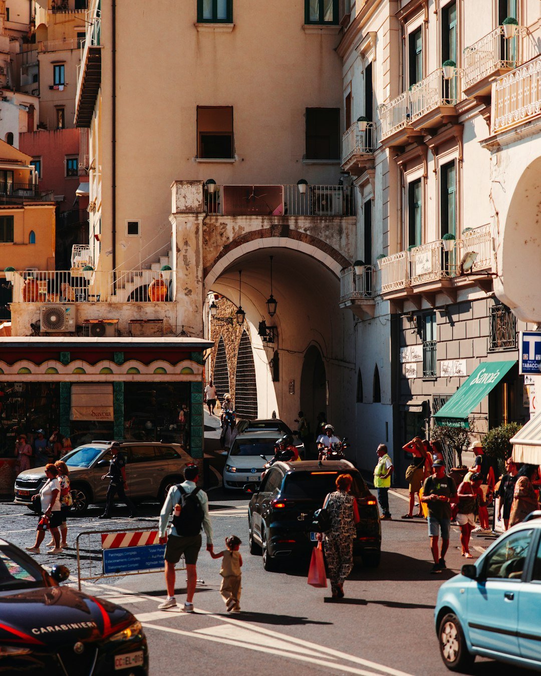 People walking on a sunny street with parked cars.