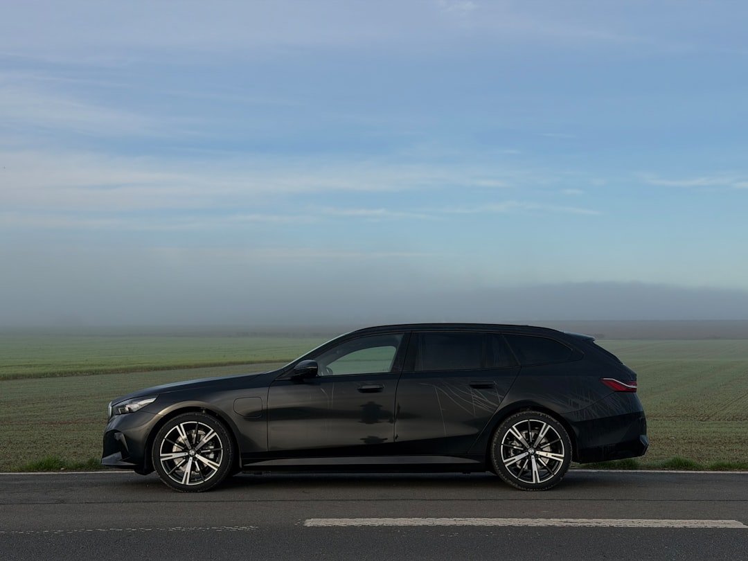 Dark station wagon parked on a road with misty fields.