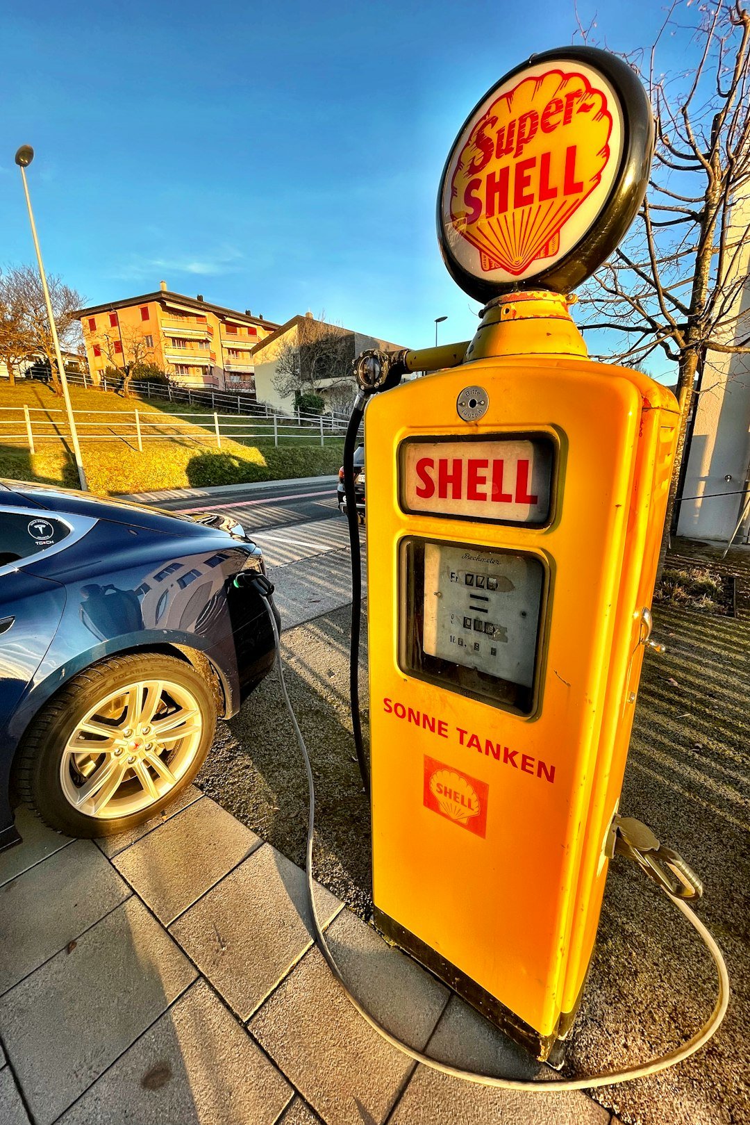 a yellow shell gas pump next to a blue car