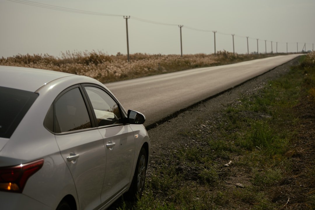 White car parked on the side of a long road