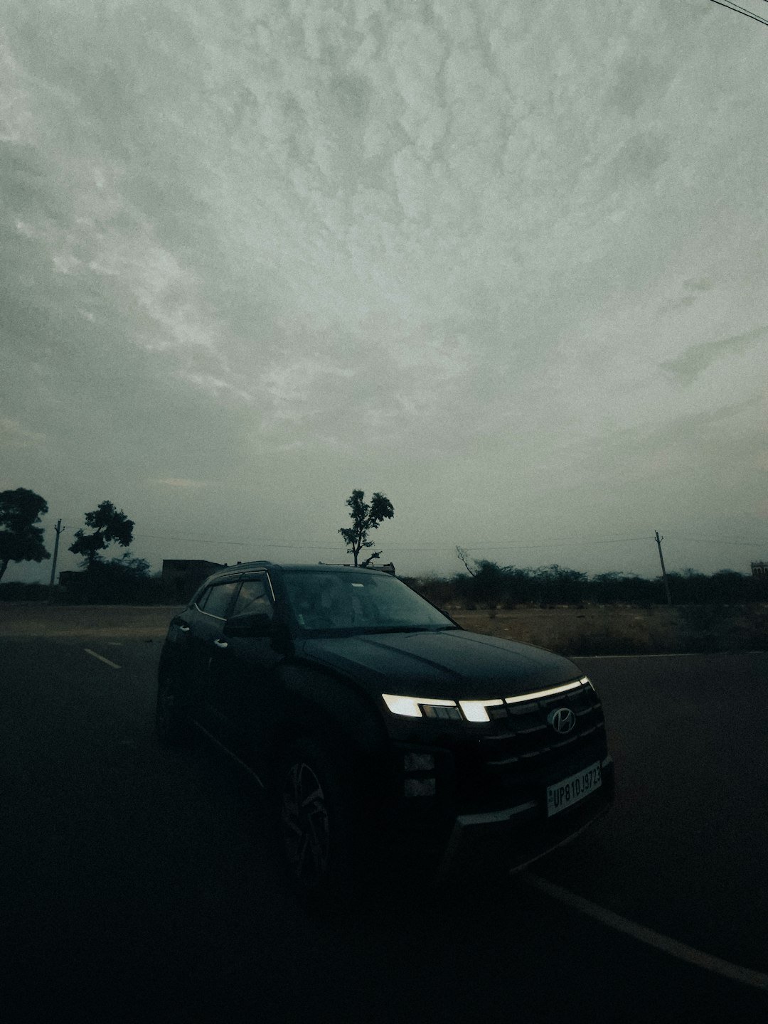 A black car is driving under a gloomy sky.