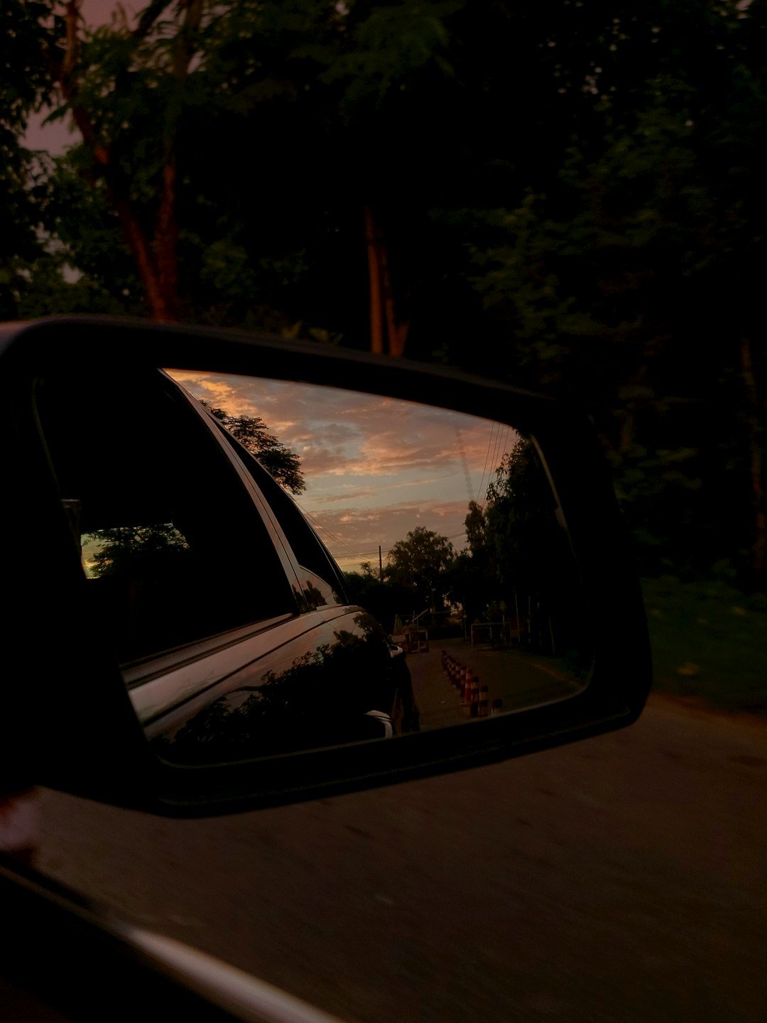 A rear view mirror on a car reflecting a sunset