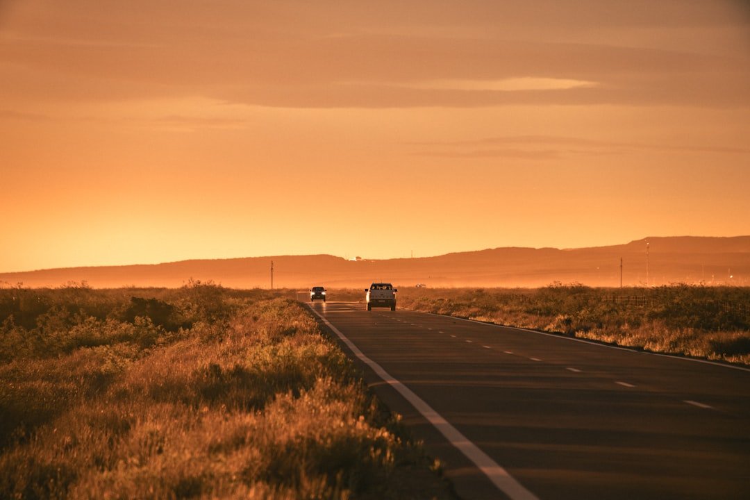 Two cars drive on a road at sunset.