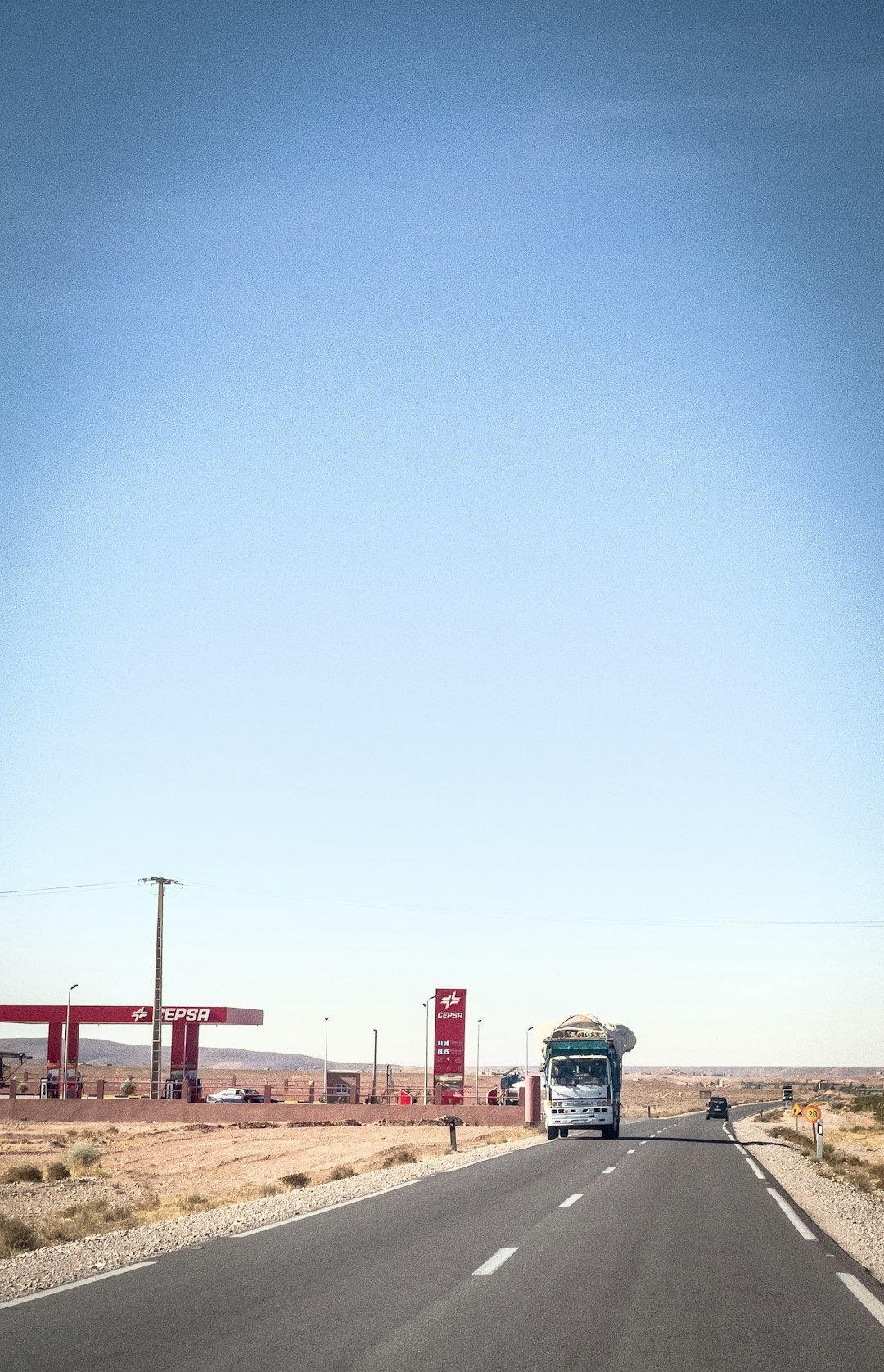 Truck driving on a desert road near a gas station.