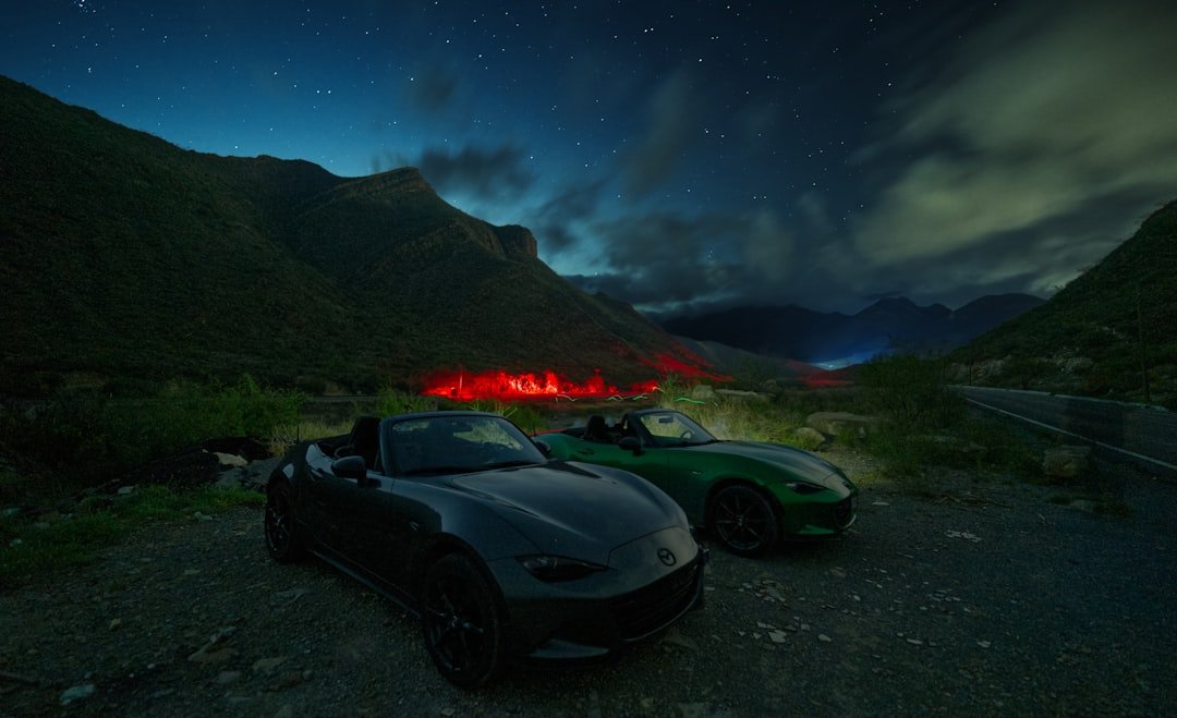 Two convertible cars parked at night with mountains.