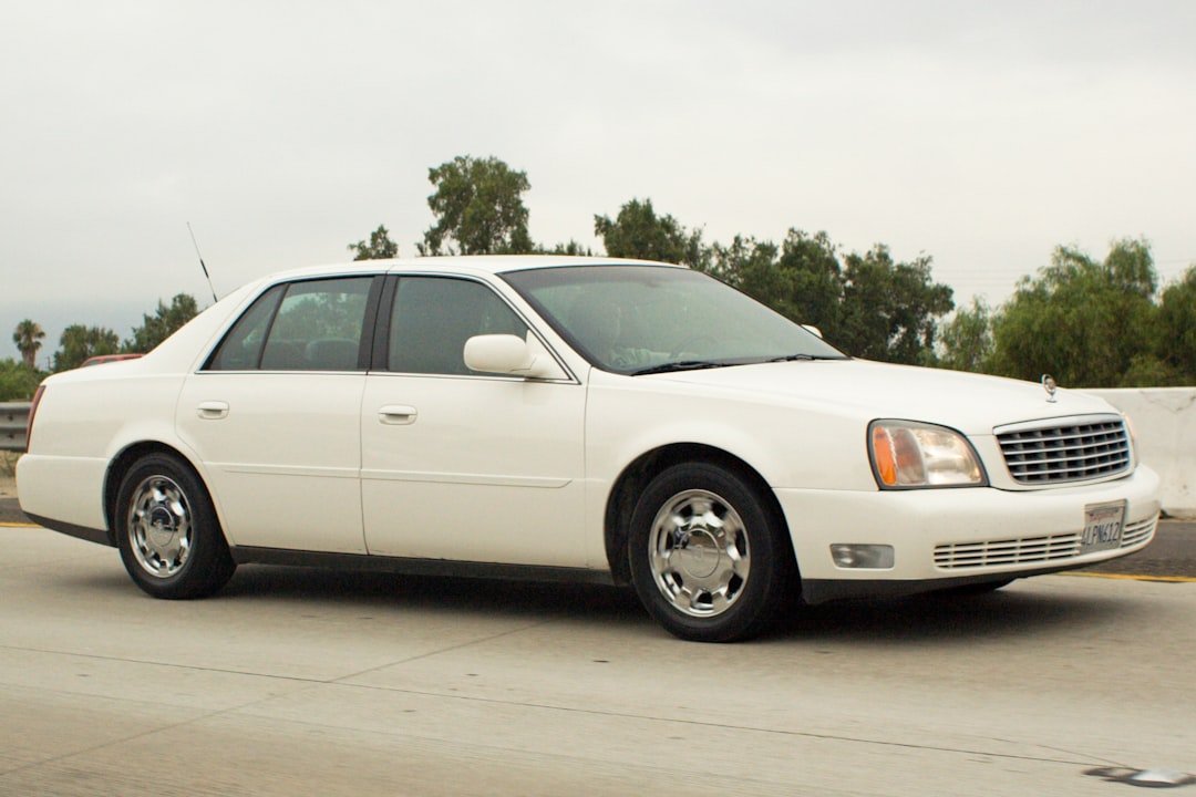 A white cadillac sedan drives on a highway.