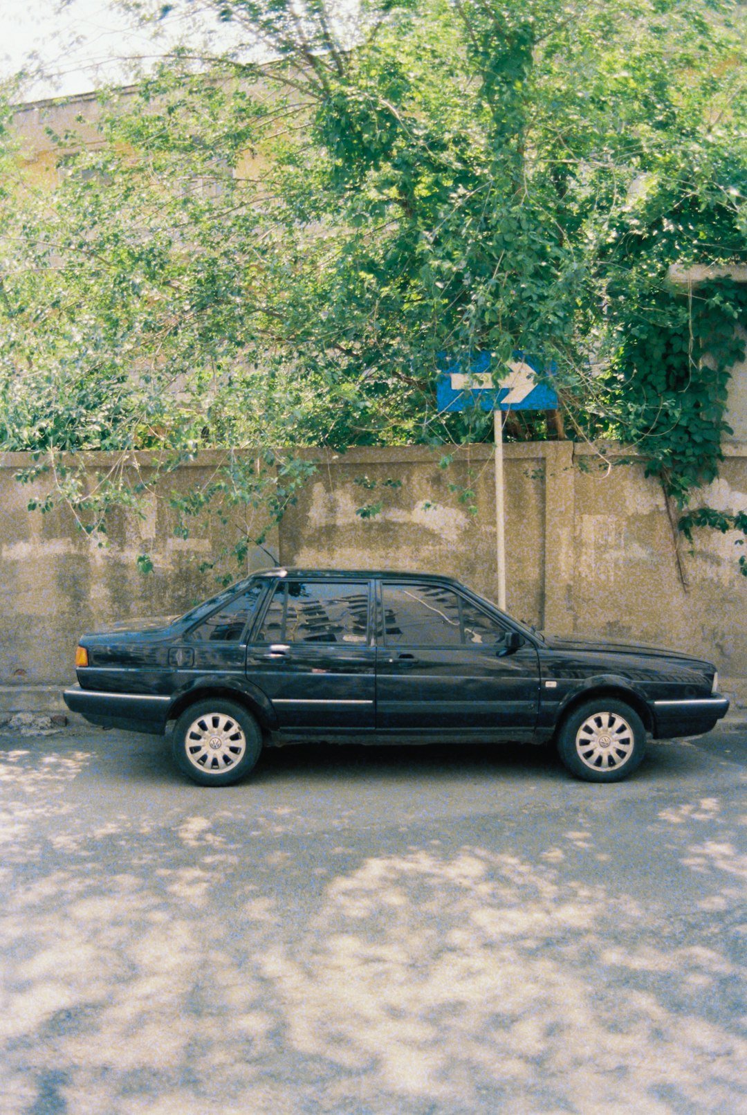 Black sedan parked on a street next to a wall.