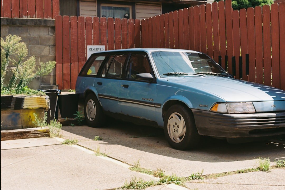 A blue car parked in front of a red fence