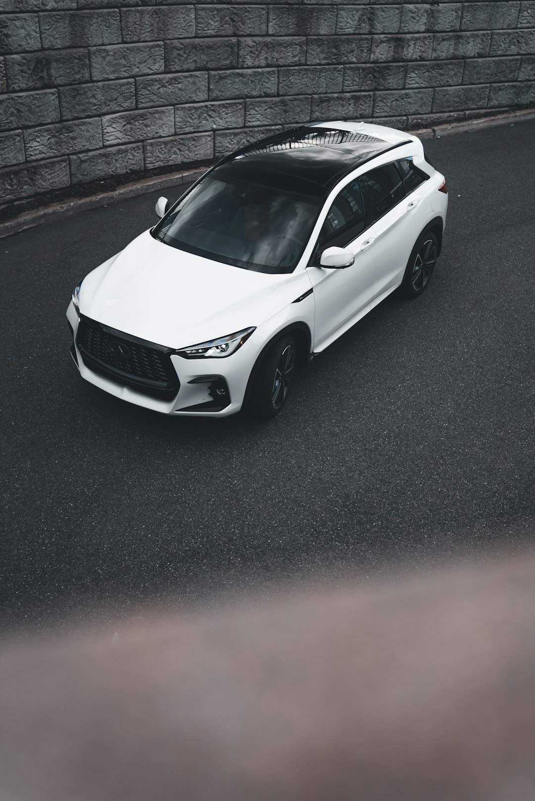 White suv parked on asphalt near brick wall.