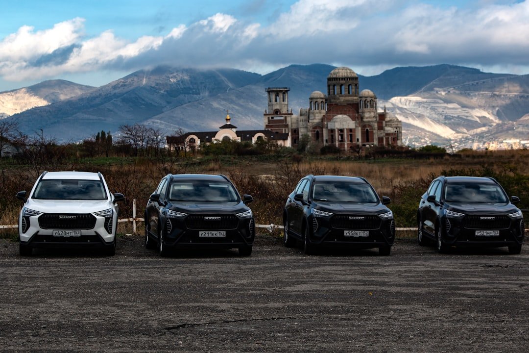 Four cars parked with a building and mountains behind.
