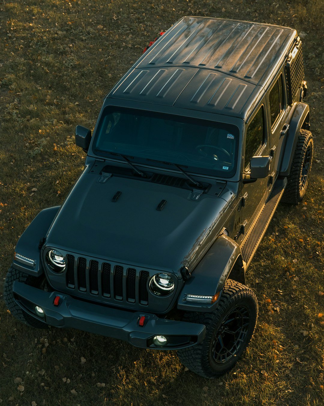 A dark grey jeep wrangler parked on grassy terrain.