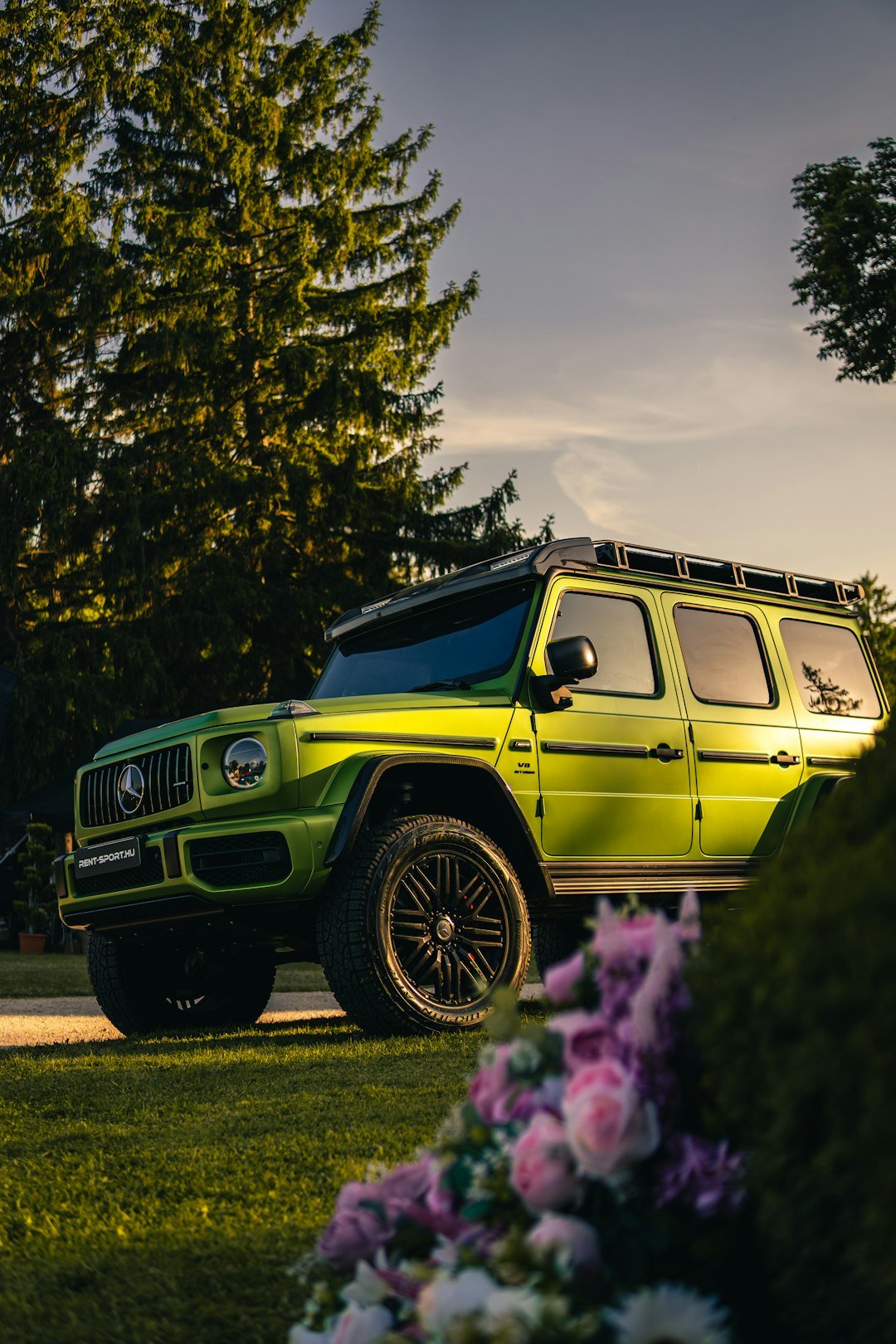 Green mercedes g-wagon parked on grassy lawn.