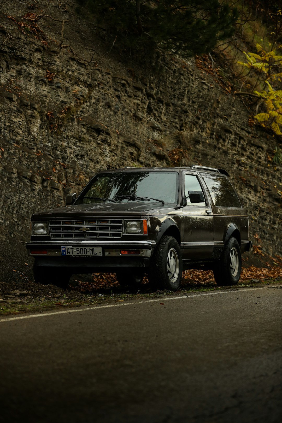 Dark suv parked on a road next to rocky hill.