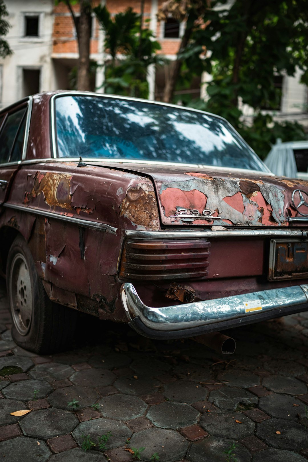 a rusted out car parked on a cobblestone street
