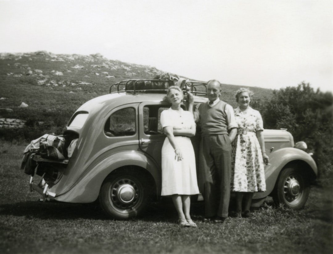 grayscale photo of 2 girls standing beside car