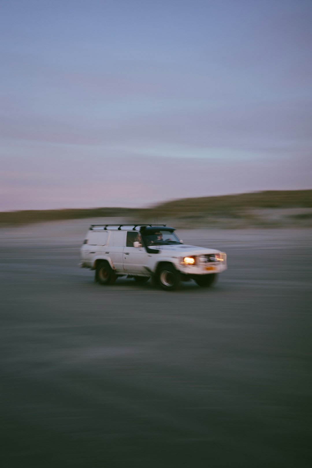 White suv driving on a sandy beach at dusk