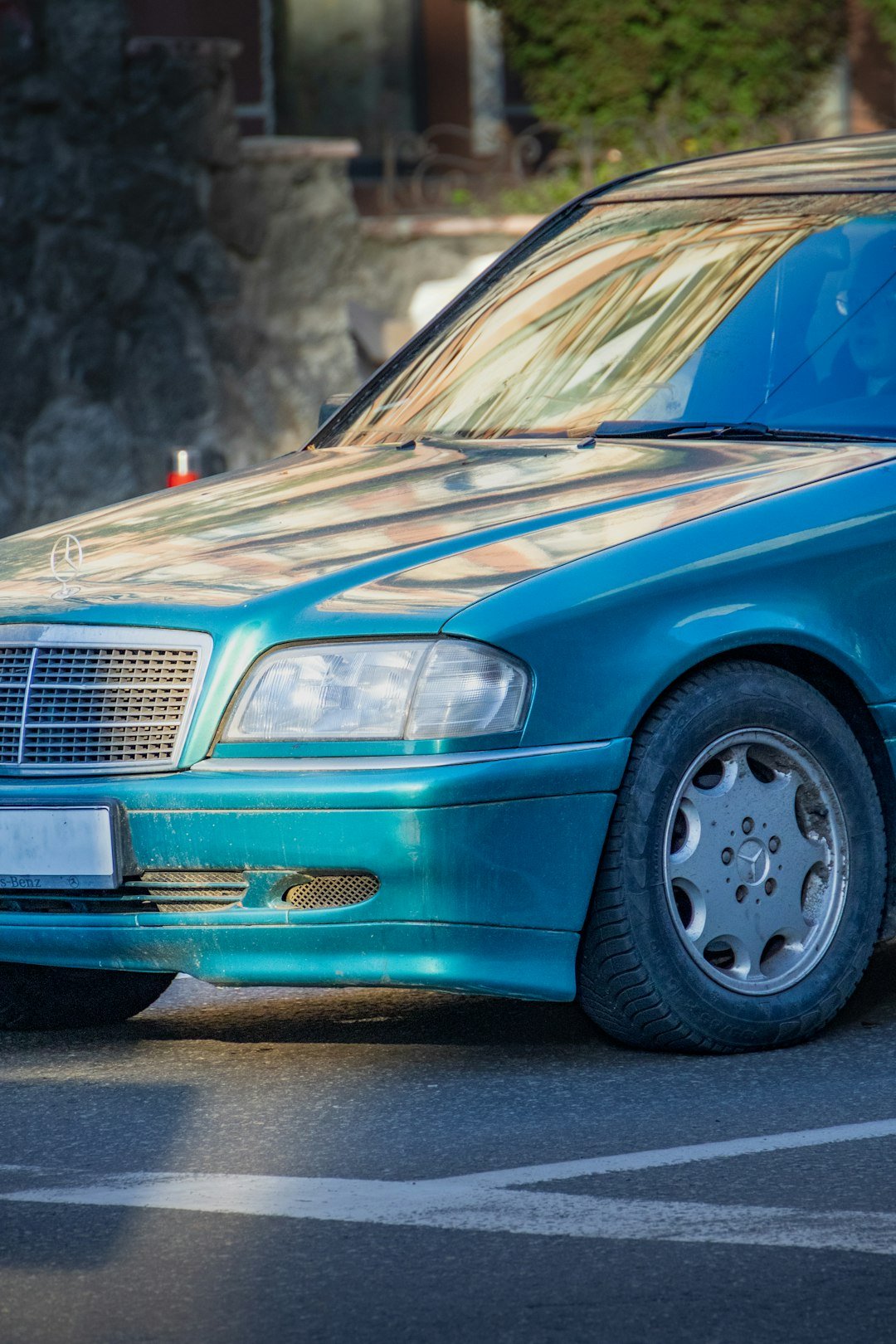 Here's a caption: a teal mercedes-benz car is parked outside.
