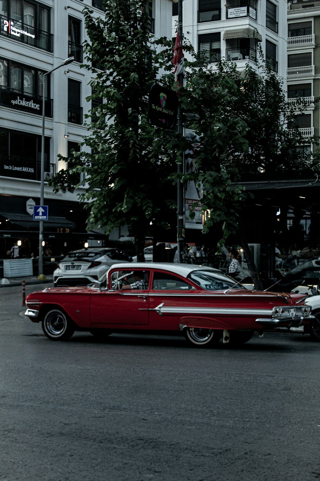 a red car driving down a street next to tall buildings