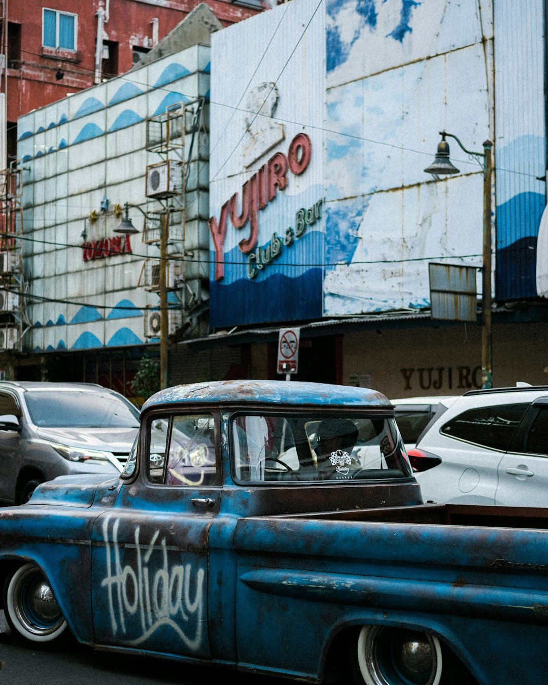 A blue truck driving down a street next to tall buildings