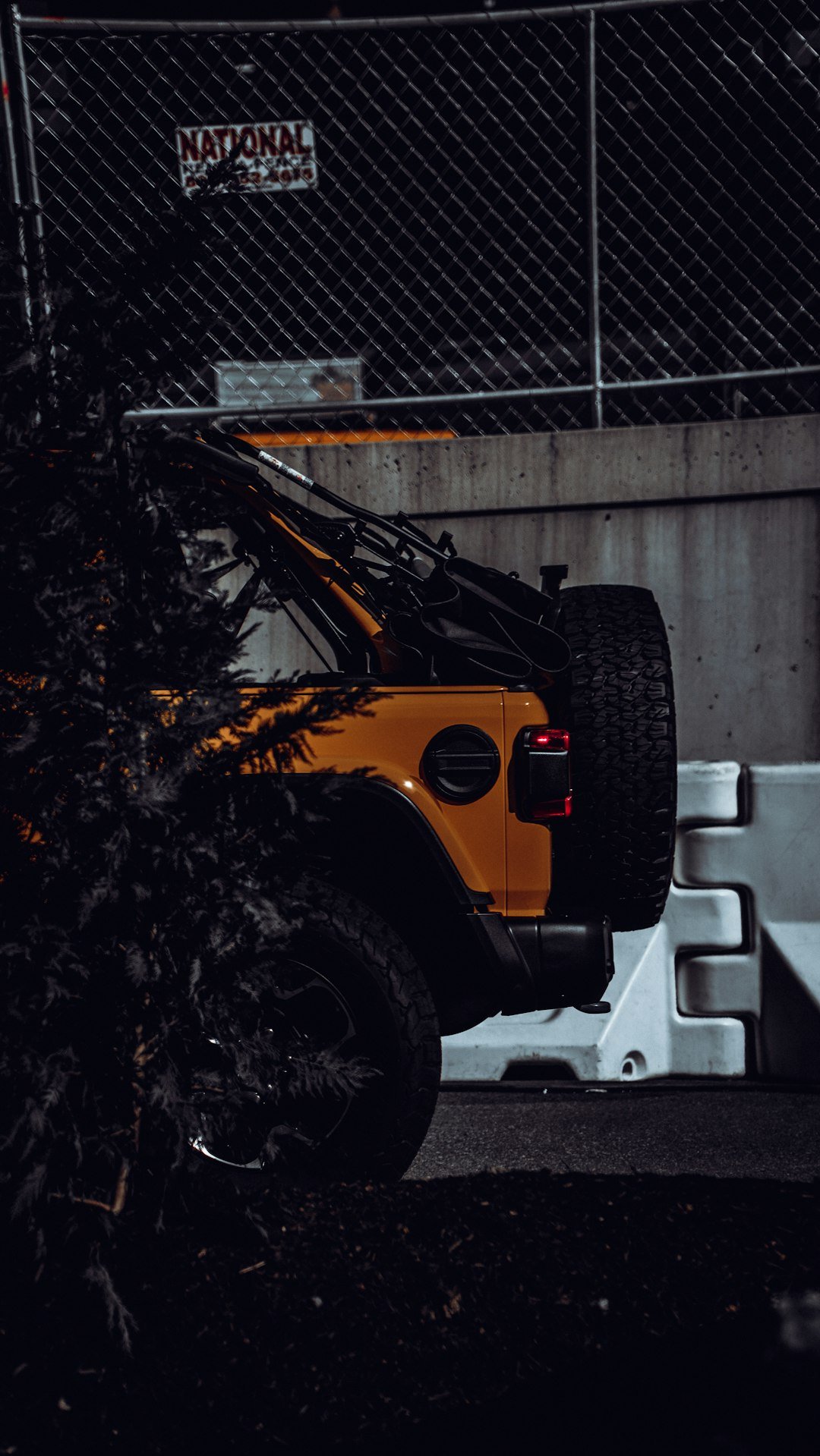 a yellow jeep parked in front of a chain link fence