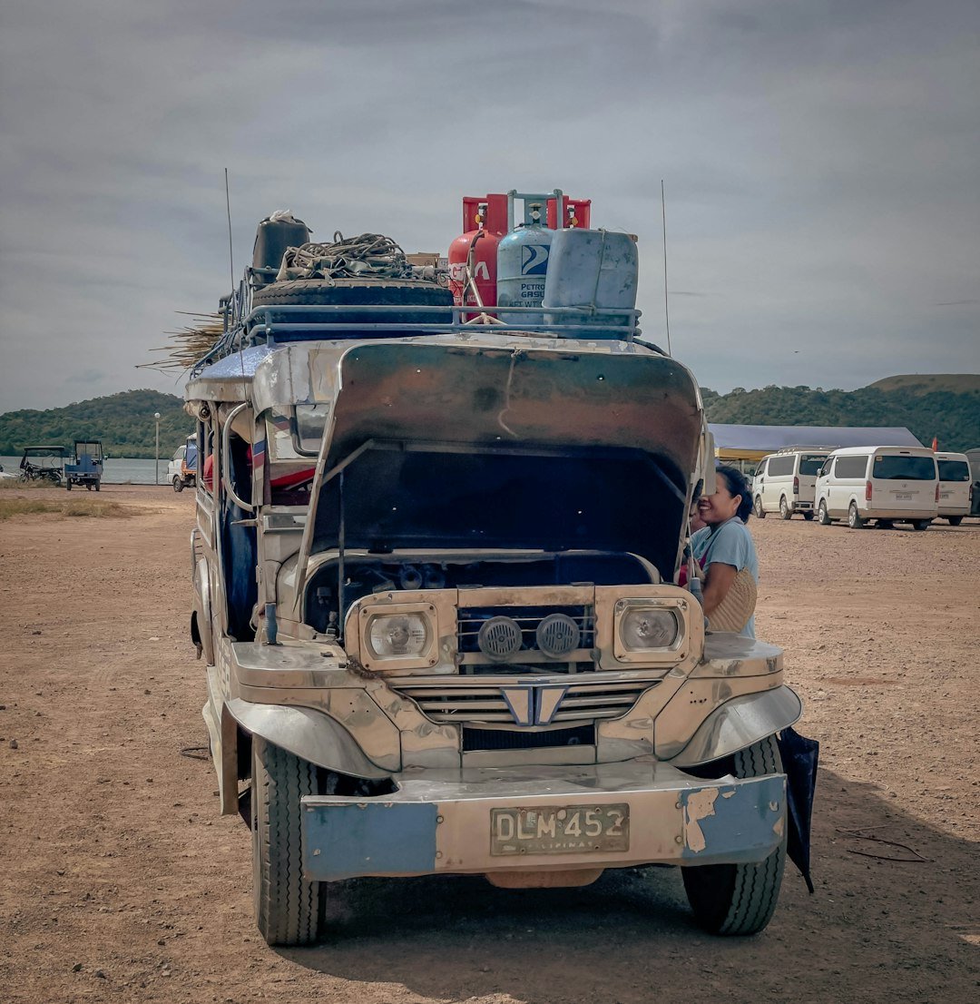 A weathered jeepney with its hood open outdoors.