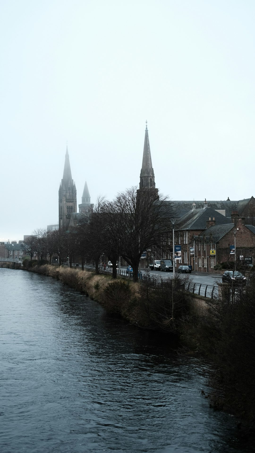 River flowing by town with church spires on foggy day