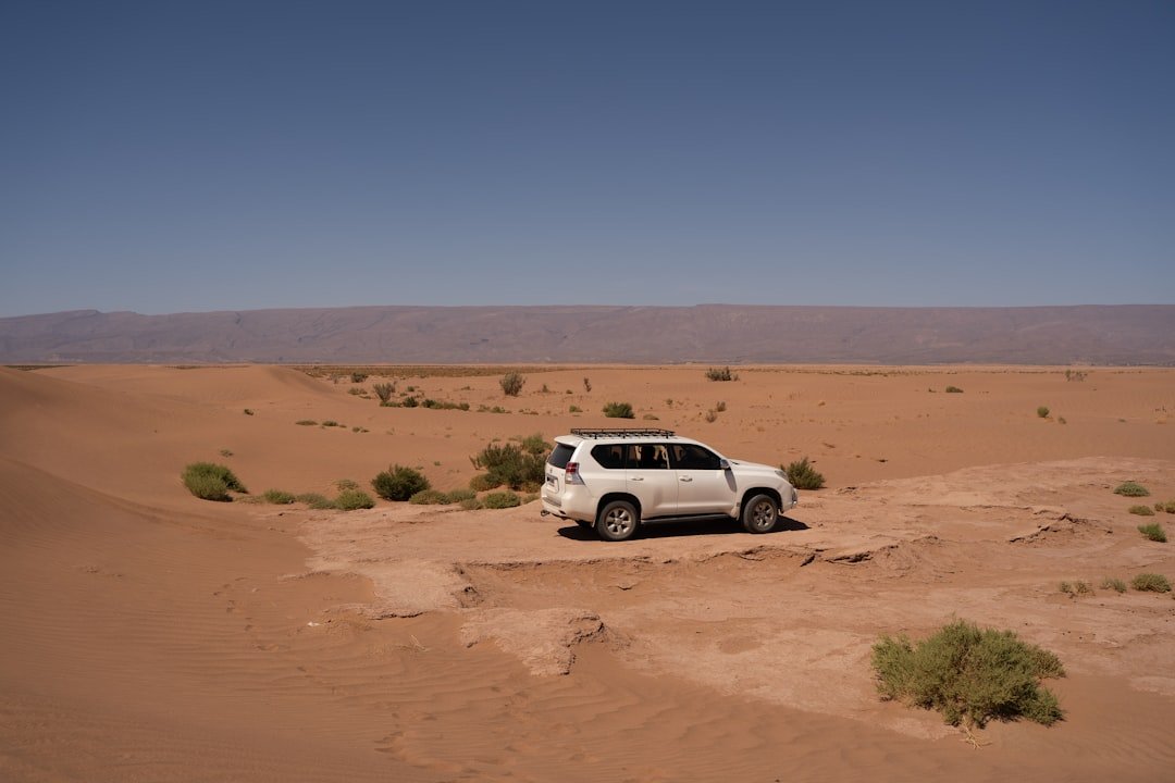 White suv parked on a sandy desert dune.
