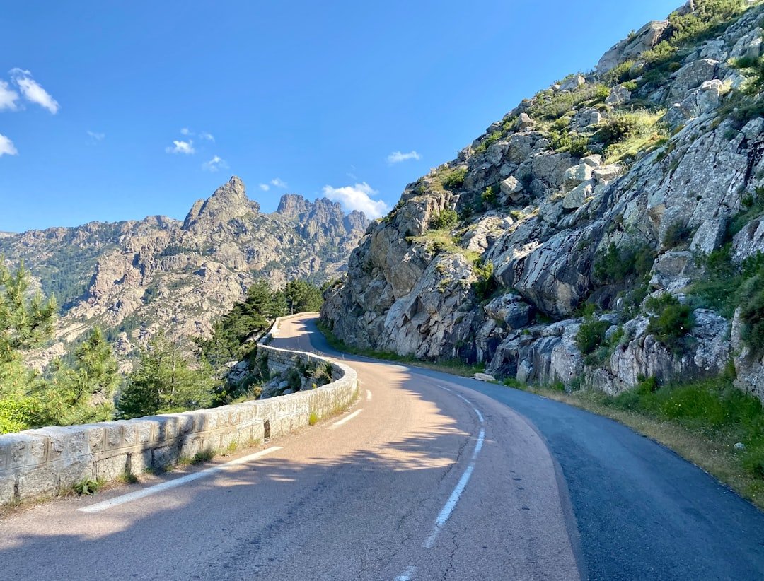 gray concrete road near green and gray mountain under blue sky during daytime