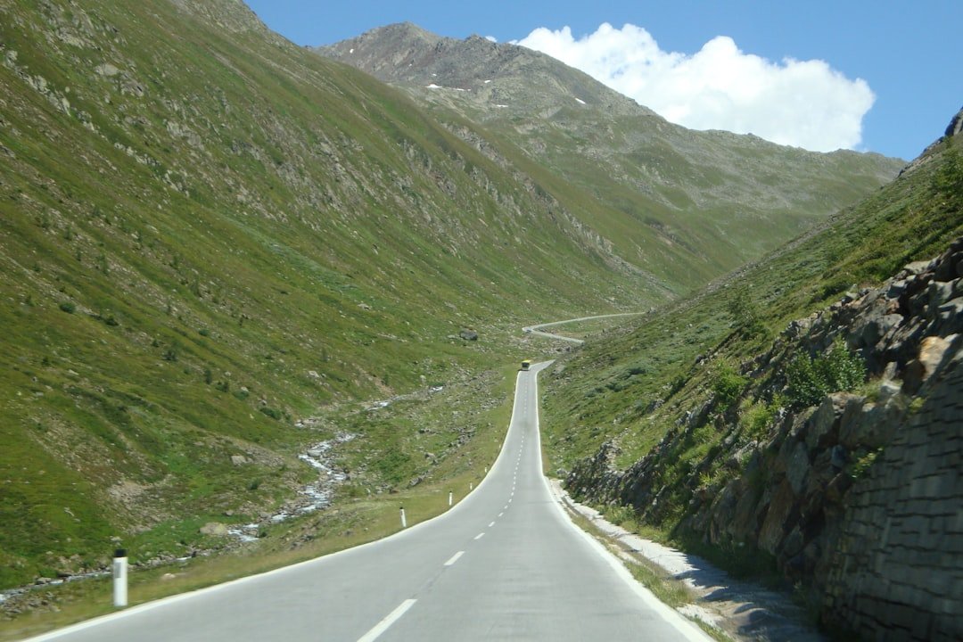 gray concrete road between green mountains during daytime
